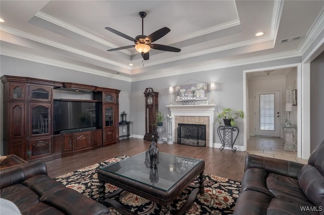 living room featuring a raised ceiling, a tiled fireplace, ceiling fan, and ornamental molding