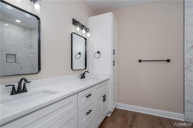 full bath with baseboards, double vanity, a sink, and wood finished floors