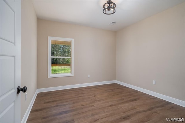 spare room with baseboards, visible vents, and dark wood-type flooring