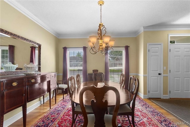 dining room with a textured ceiling, ornamental molding, light wood-type flooring, and a notable chandelier