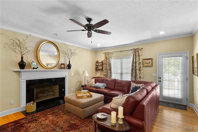 living room with a tile fireplace, a textured ceiling, hardwood / wood-style floors, ceiling fan, and ornamental molding