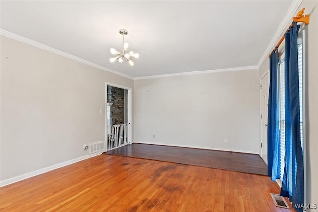 spare room with ornamental molding, visible vents, a notable chandelier, and wood finished floors