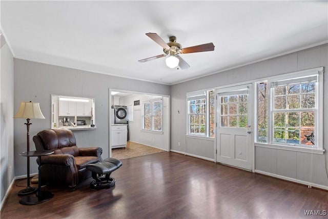 sitting room featuring a wealth of natural light, a ceiling fan, dark wood-type flooring, and stacked washer / dryer