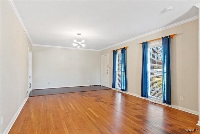 spare room featuring a chandelier, ornamental molding, baseboards, and wood finished floors