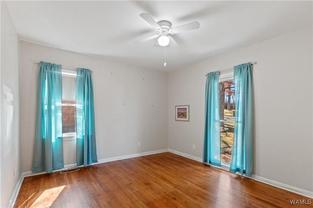 unfurnished room featuring baseboards, wood finished floors, visible vents, and a ceiling fan