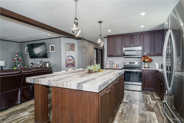 kitchen featuring decorative light fixtures, a textured ceiling, dark hardwood / wood-style floors, stainless steel appliances, and a kitchen island with sink