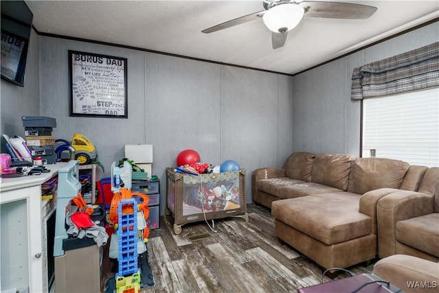 rec room with dark wood-type flooring, ornamental molding, and ceiling fan