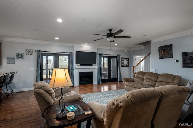 living room featuring dark wood-type flooring, a large fireplace, ornamental molding, and french doors