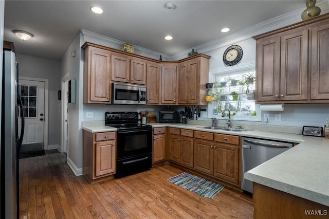 kitchen with stainless steel appliances, wood-type flooring, sink, and ornamental molding