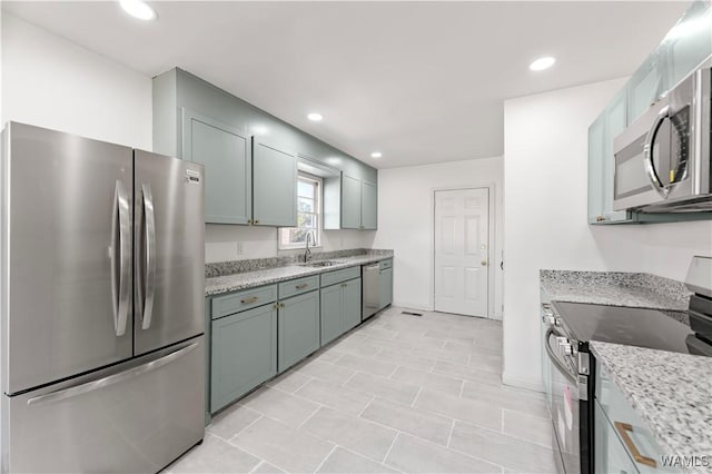 kitchen with light stone countertops, stainless steel appliances, a sink, and recessed lighting