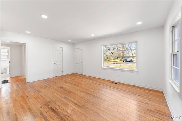 unfurnished room with light wood-type flooring, visible vents, and a healthy amount of sunlight