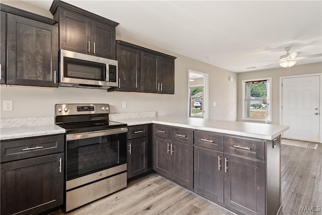 kitchen with stainless steel appliances, kitchen peninsula, light wood-type flooring, ceiling fan, and dark brown cabinets