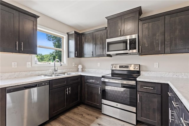 kitchen with hardwood / wood-style floors, sink, dark brown cabinetry, appliances with stainless steel finishes, and light stone counters