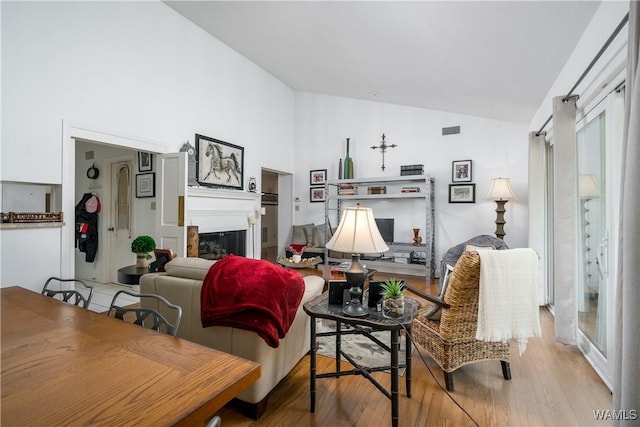 living area featuring high vaulted ceiling, a fireplace, visible vents, and wood finished floors