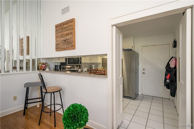 kitchen with visible vents, a breakfast bar, stainless steel appliances, light countertops, and light tile patterned flooring