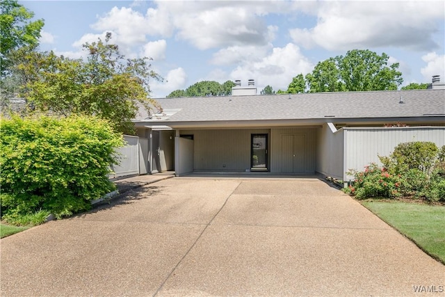 view of front of house featuring a chimney, concrete driveway, and roof with shingles