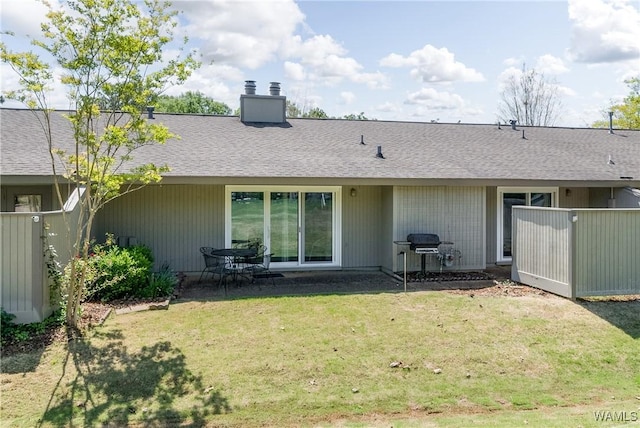 rear view of property featuring a shingled roof, a chimney, fence, and a lawn