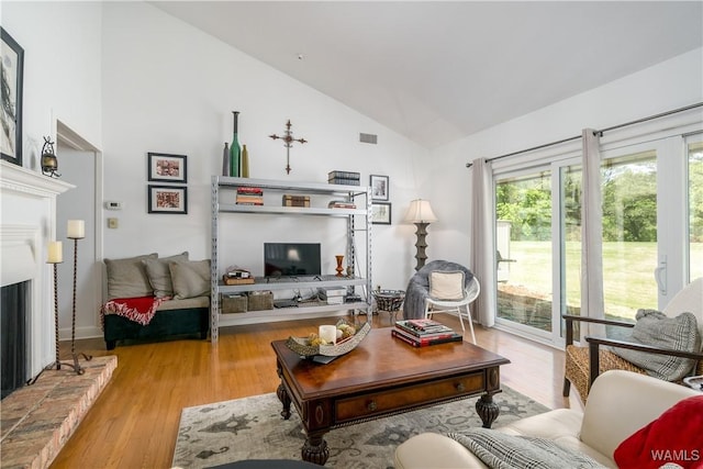 living area featuring a fireplace with raised hearth, visible vents, vaulted ceiling, and wood finished floors