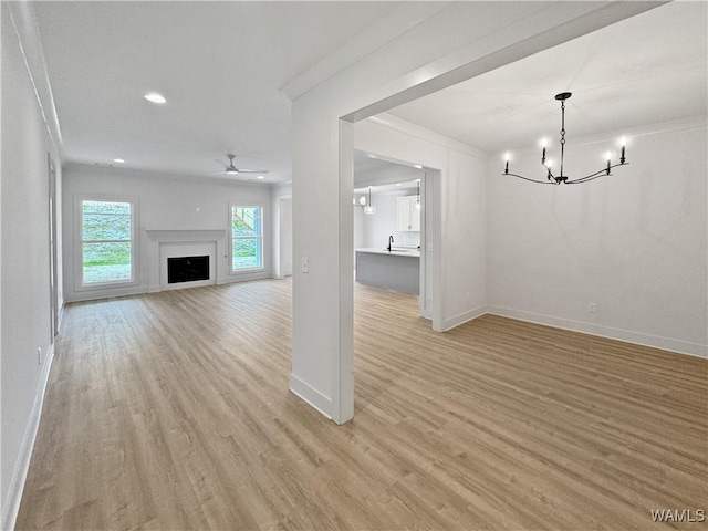 unfurnished living room with crown molding, sink, ceiling fan with notable chandelier, and light hardwood / wood-style flooring