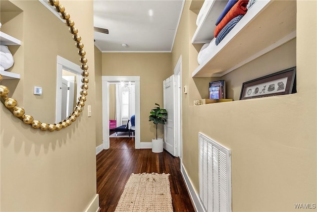 hall featuring baseboards, crown molding, visible vents, and wood finished floors