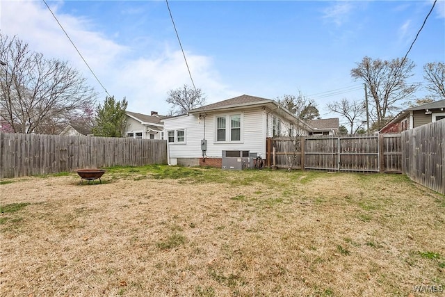 back of house with an outdoor fire pit, a fenced backyard, a lawn, and central AC unit