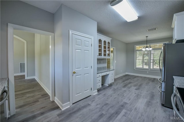 kitchen featuring hardwood / wood-style floors, pendant lighting, an inviting chandelier, white cabinets, and stainless steel fridge