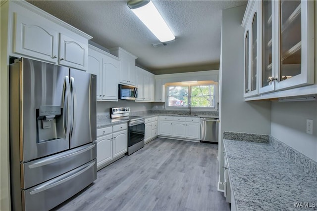 kitchen with sink, light stone countertops, a textured ceiling, white cabinetry, and stainless steel appliances