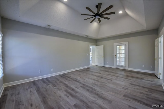 empty room with wood-type flooring, a textured ceiling, a tray ceiling, and ceiling fan