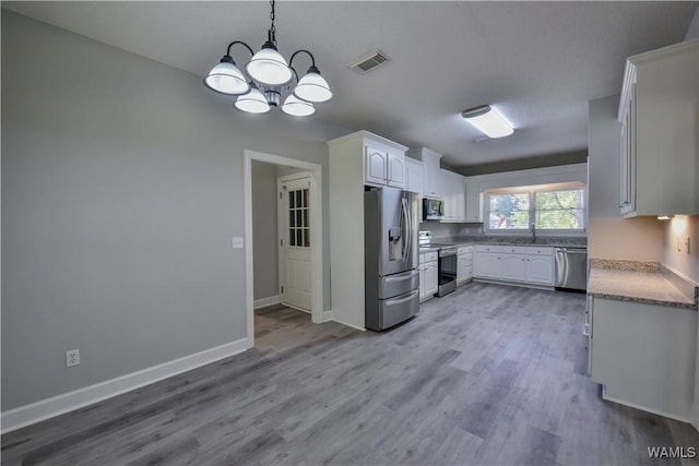 kitchen with an inviting chandelier, hanging light fixtures, light wood-type flooring, appliances with stainless steel finishes, and white cabinetry