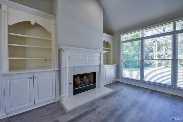 unfurnished living room featuring a tile fireplace, built in shelves, and dark wood-type flooring