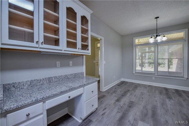 kitchen featuring a textured ceiling, light stone counters, white cabinets, and decorative light fixtures