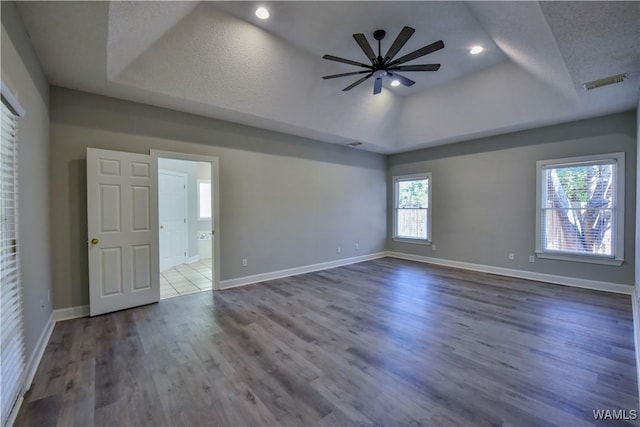 empty room with a tray ceiling, ceiling fan, hardwood / wood-style floors, and a textured ceiling