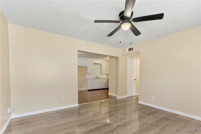 empty room featuring a textured ceiling, light wood-type flooring, ceiling fan, and sink