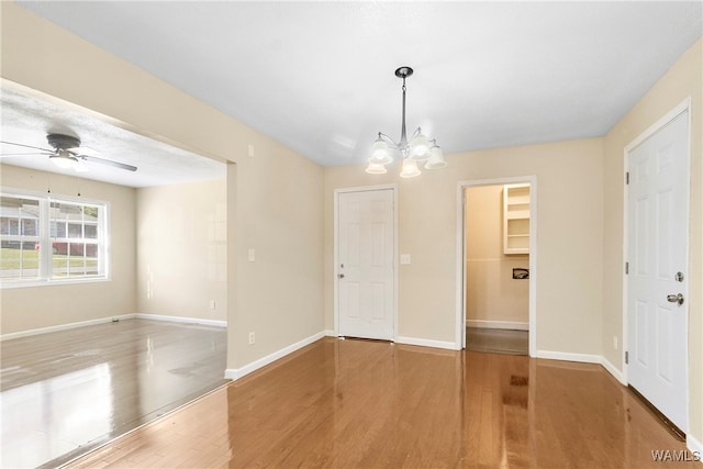 empty room with ceiling fan with notable chandelier and hardwood / wood-style flooring