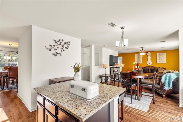 kitchen featuring an inviting chandelier, light hardwood / wood-style flooring, decorative light fixtures, a kitchen island, and light stone counters