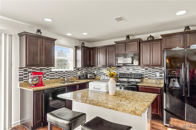 kitchen with decorative backsplash, light stone countertops, sink, black appliances, and a kitchen island