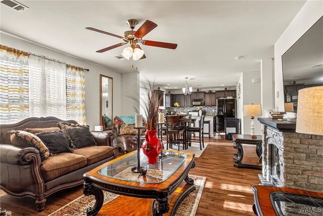 living room featuring a stone fireplace, light hardwood / wood-style flooring, and ceiling fan with notable chandelier