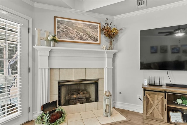 living room featuring baseboards, visible vents, a tiled fireplace, ornamental molding, and wood finished floors