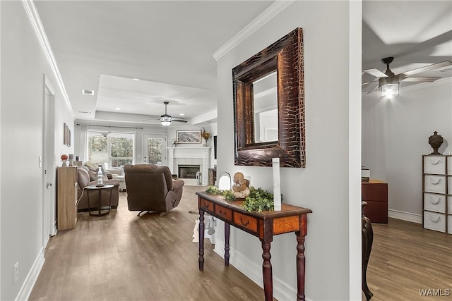 hallway with baseboards, visible vents, ornamental molding, wood finished floors, and a tray ceiling