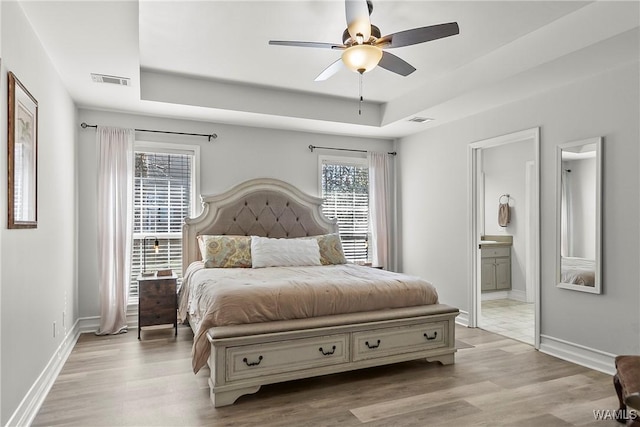 bedroom with light wood finished floors, a tray ceiling, multiple windows, and visible vents