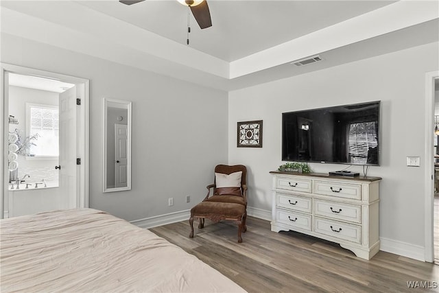 bedroom with a tray ceiling, wood finished floors, visible vents, and baseboards