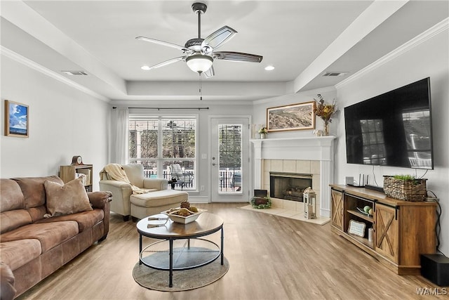 living area featuring ornamental molding, light wood-type flooring, a raised ceiling, and visible vents