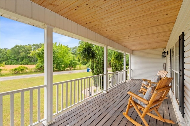 wooden terrace with a lawn, covered porch, and view of scattered trees