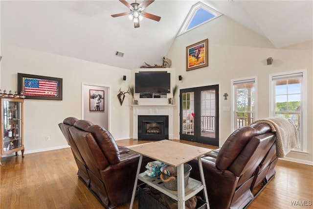 living room with a ceiling fan, high vaulted ceiling, a glass covered fireplace, baseboards, and wood finished floors