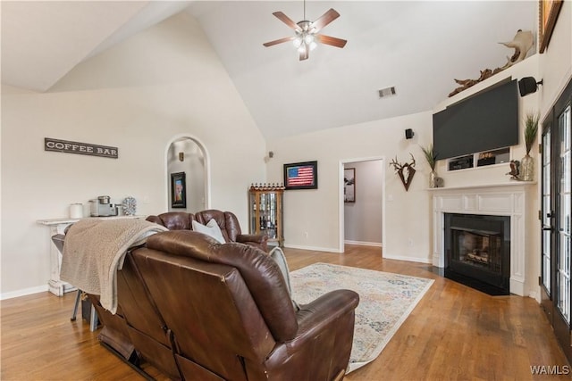 living room featuring a ceiling fan, high vaulted ceiling, a fireplace with flush hearth, wood finished floors, and baseboards