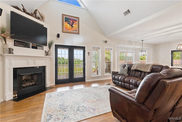 living room with light wood-type flooring, a fireplace with flush hearth, high vaulted ceiling, and french doors