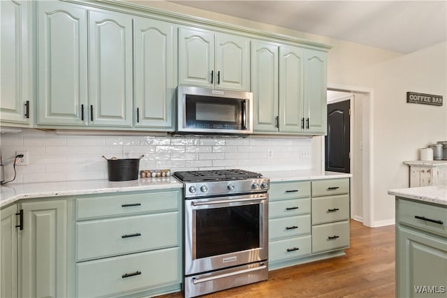 kitchen featuring appliances with stainless steel finishes, wood finished floors, backsplash, and green cabinetry