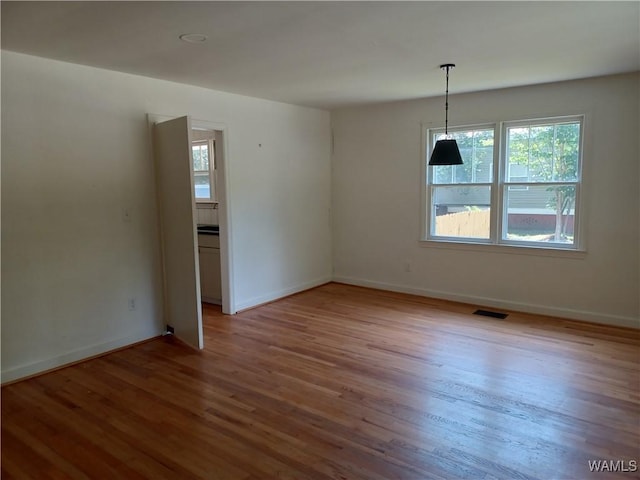 empty room with wood finished floors, visible vents, and baseboards