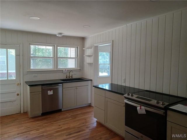 kitchen with dark countertops, appliances with stainless steel finishes, light wood-style floors, open shelves, and a sink