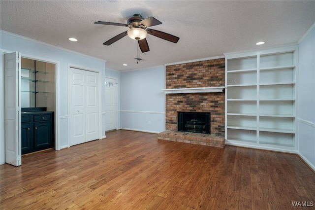 unfurnished living room with a brick fireplace, a textured ceiling, ceiling fan, crown molding, and wood-type flooring